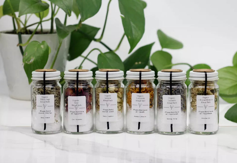 Set of clear glass bath salt jars with white screw lids and front ingredient labels.