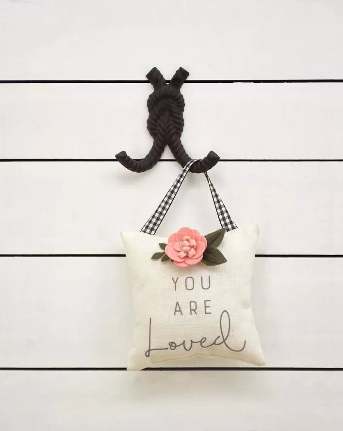 Rope-style cast iron wall hook holding a fabric love pillow with flower