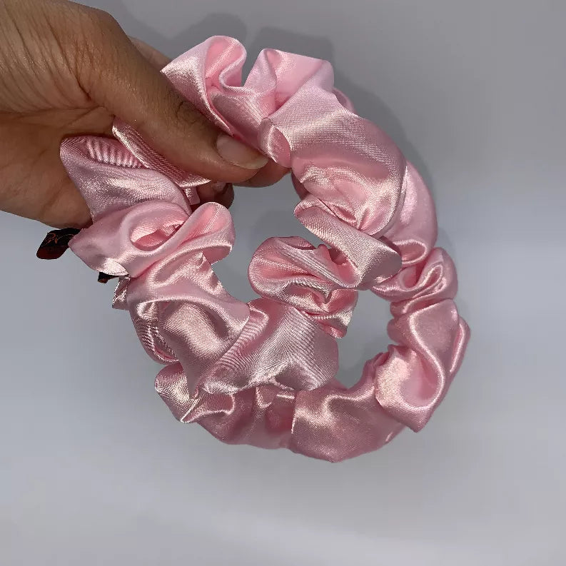 Hand holding two pink satin scrunchies with gathered ruffle loops