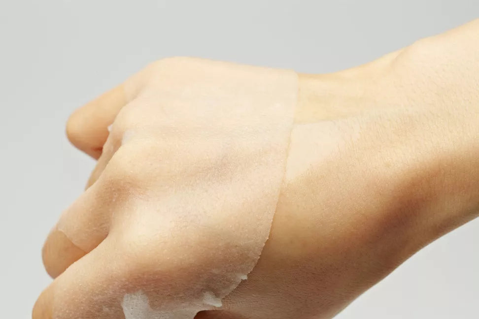 Sheet mask applied on forearm with thin translucent sheet and folded edges.