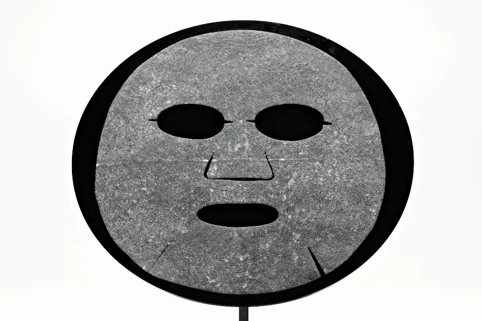 Close-up of a gray face mask sheet with cutout eye and mouth shapes.