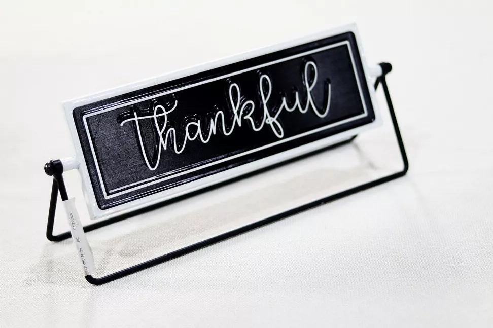 Rotating tabletop metal sign angled view, black panel with white cursive 'Thankful' text