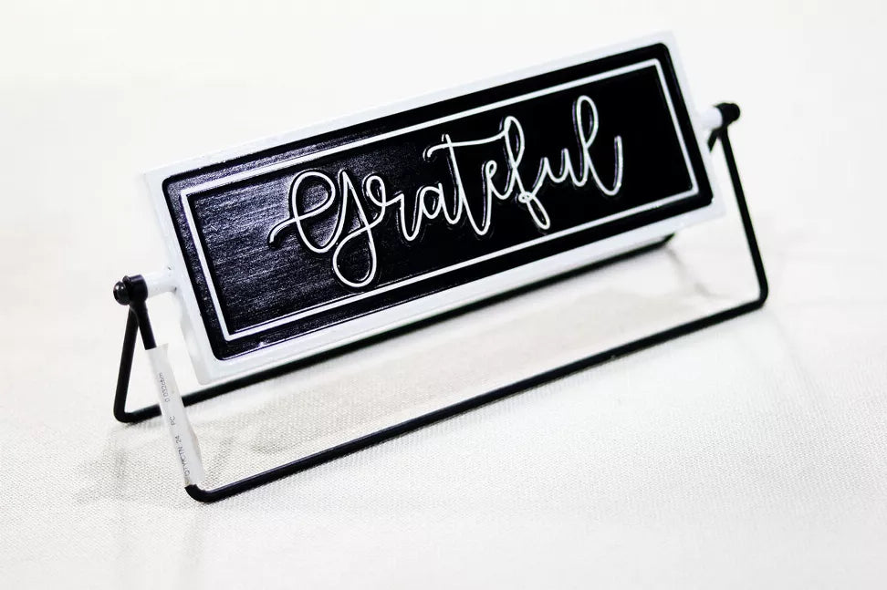 Rotating tabletop metal sign angled view, black panel with white cursive 'Grateful' text