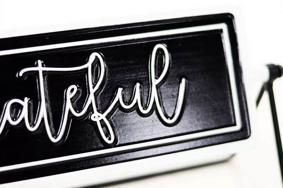 Close-up rotating metal tabletop sign showing white cursive 'Thankful' on black panel