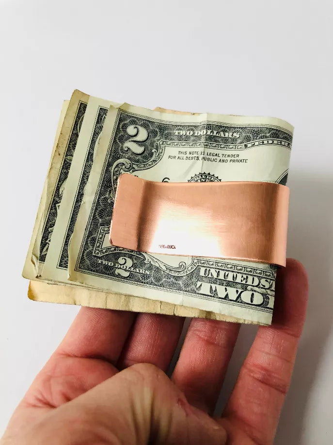 Copper money clip holding several folded US dollar bills