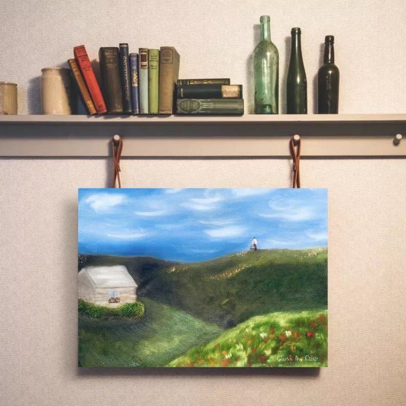 Landscape art print hanging with green hills, white cottage, and red flowers under blue sky