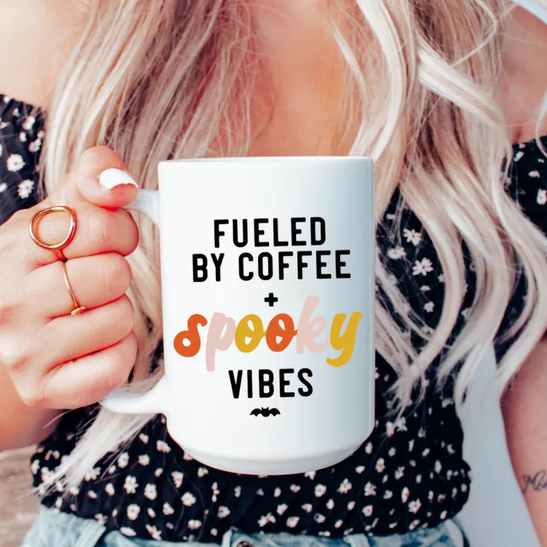 White ceramic coffee mug with black and orange 'Fueled by coffee spooky vibes' text