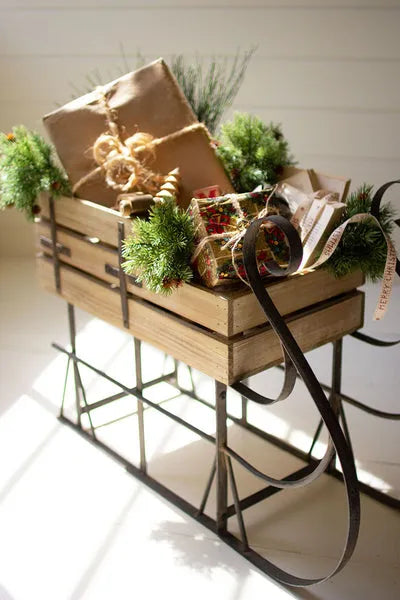 Brown wooden Christmas sled with metal runners, green garland, wrapped gifts and ribbon