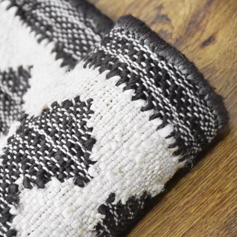 Jute kilim rug corner with fringe and woven texture, black and ivory pattern.