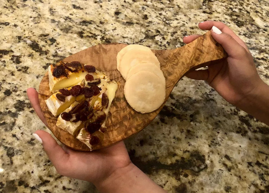 Olive wood cutting board with curved handle, held with food slices on top