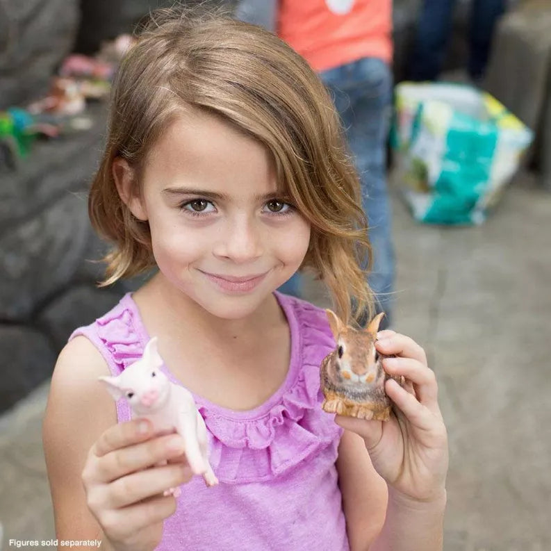 Pink piglet figurine held by child in purple dress, beside small animal