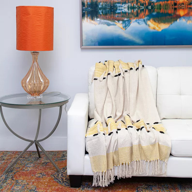 Cream and yellow throw blanket with black paw prints and tasseled fringe, draped