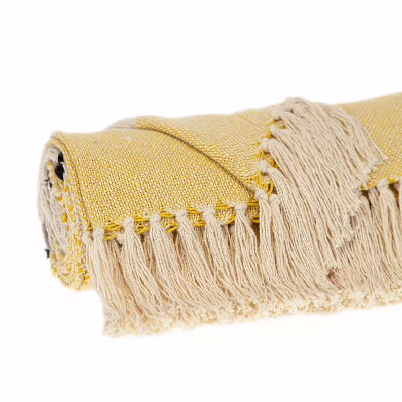 Corner of yellow and cream throw blanket with black paw prints and fringe tassels