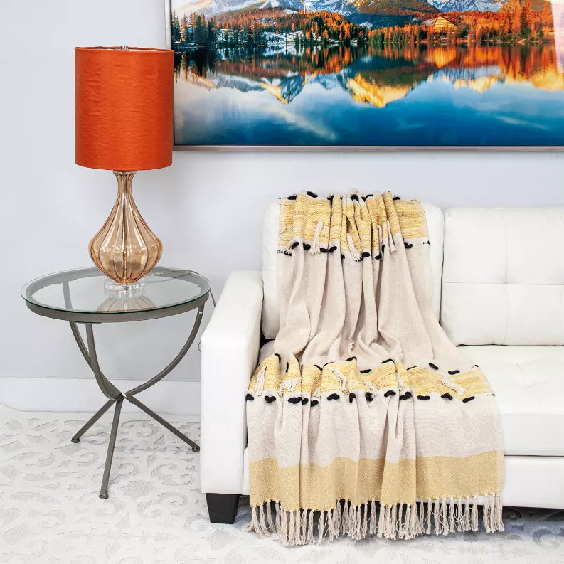 Cream and yellow throw blanket with black paw prints and fringe, draped on sofa