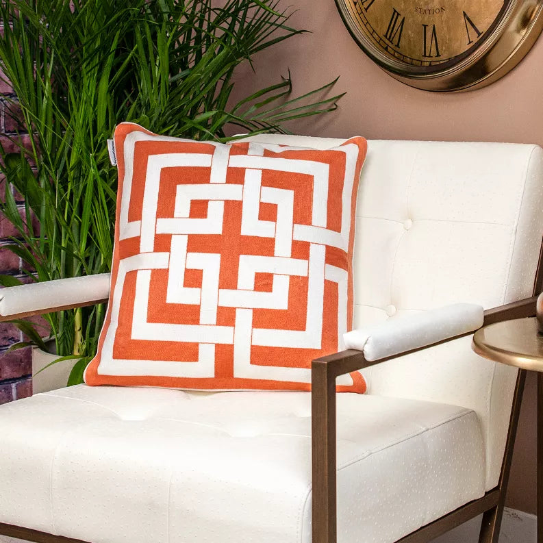 Orange and white geometric throw pillow on an upholstered chair