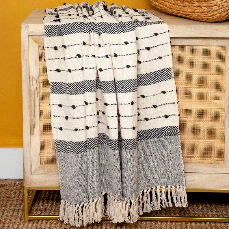 Woven handloom throw draped on furniture, cream with dark gray geometric bands and tassels