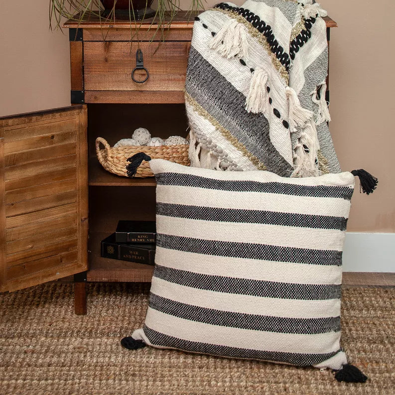 Beige and black striped pillow cover with tassels, set on a bed, 24 x 24