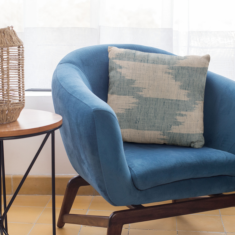 Throw pillow on blue armchair: blue-and-cream abstract rectangle with faded horizontal bands.