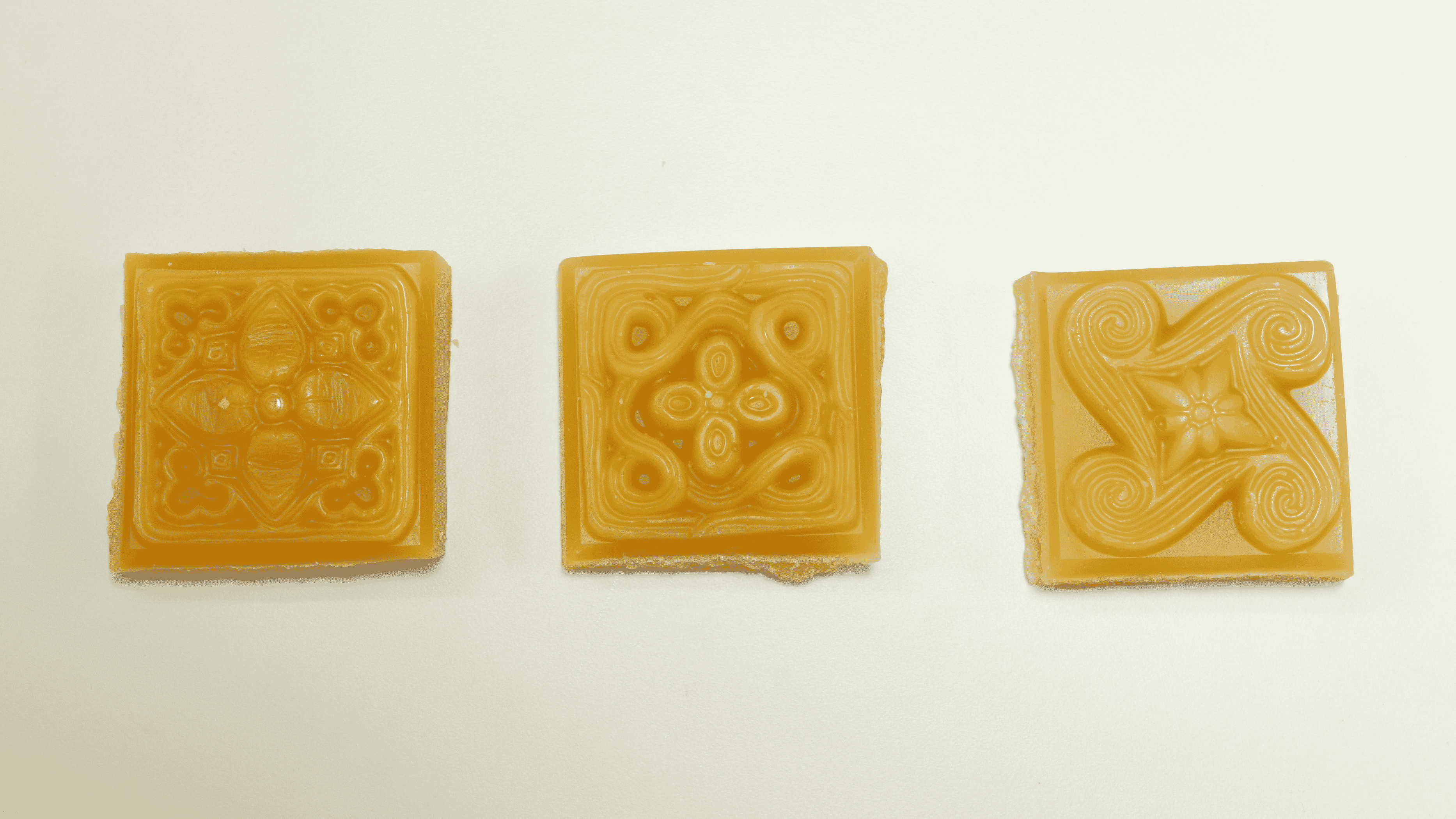 Three amber beeswax soap squares with different embossed decorative patterns