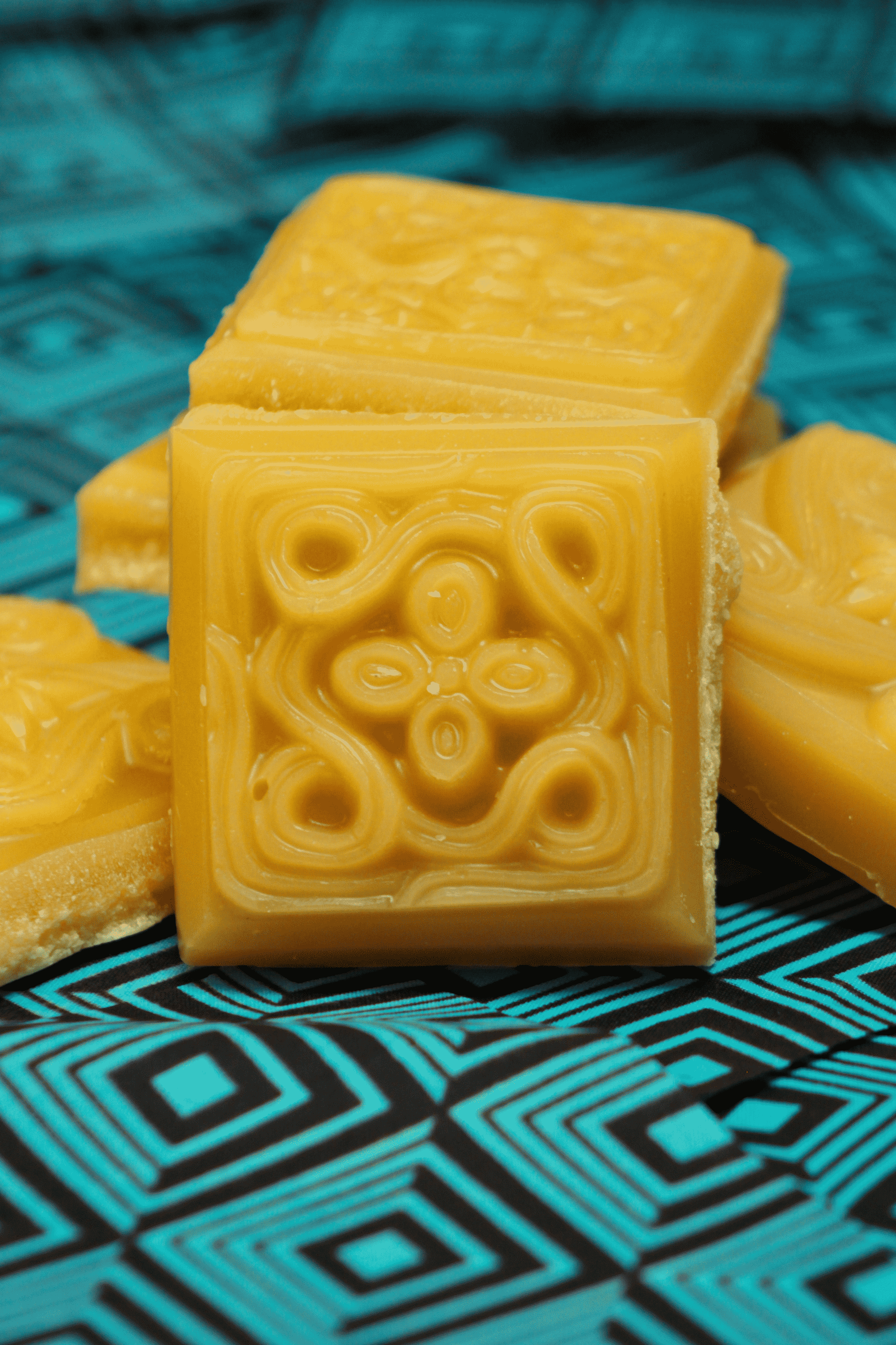 Amber beeswax soap bars with embossed swirl pattern, stacked on teal cloth