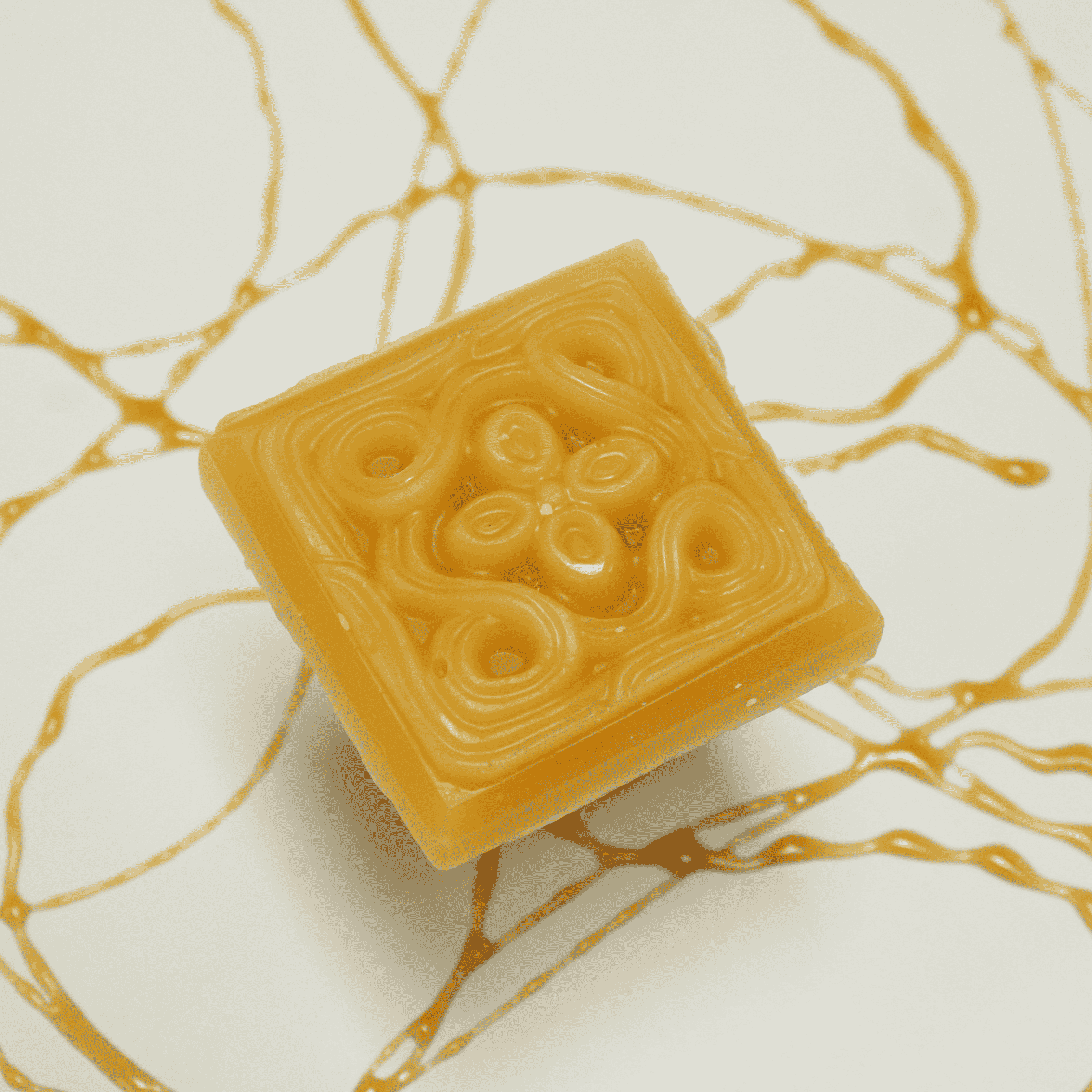Amber beeswax soap bar with embossed swirl-and-circle pattern