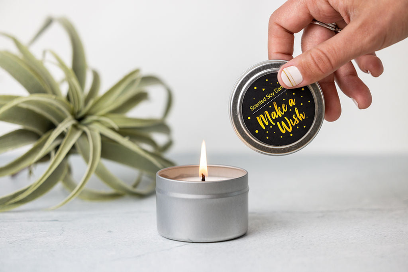 Scented soy candle in gray tin with wick lit and lid held in hand