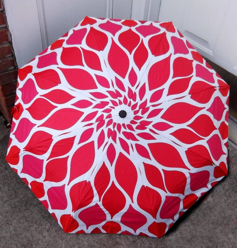 Compact umbrella, open canopy with red and white organic petal pattern and center button.