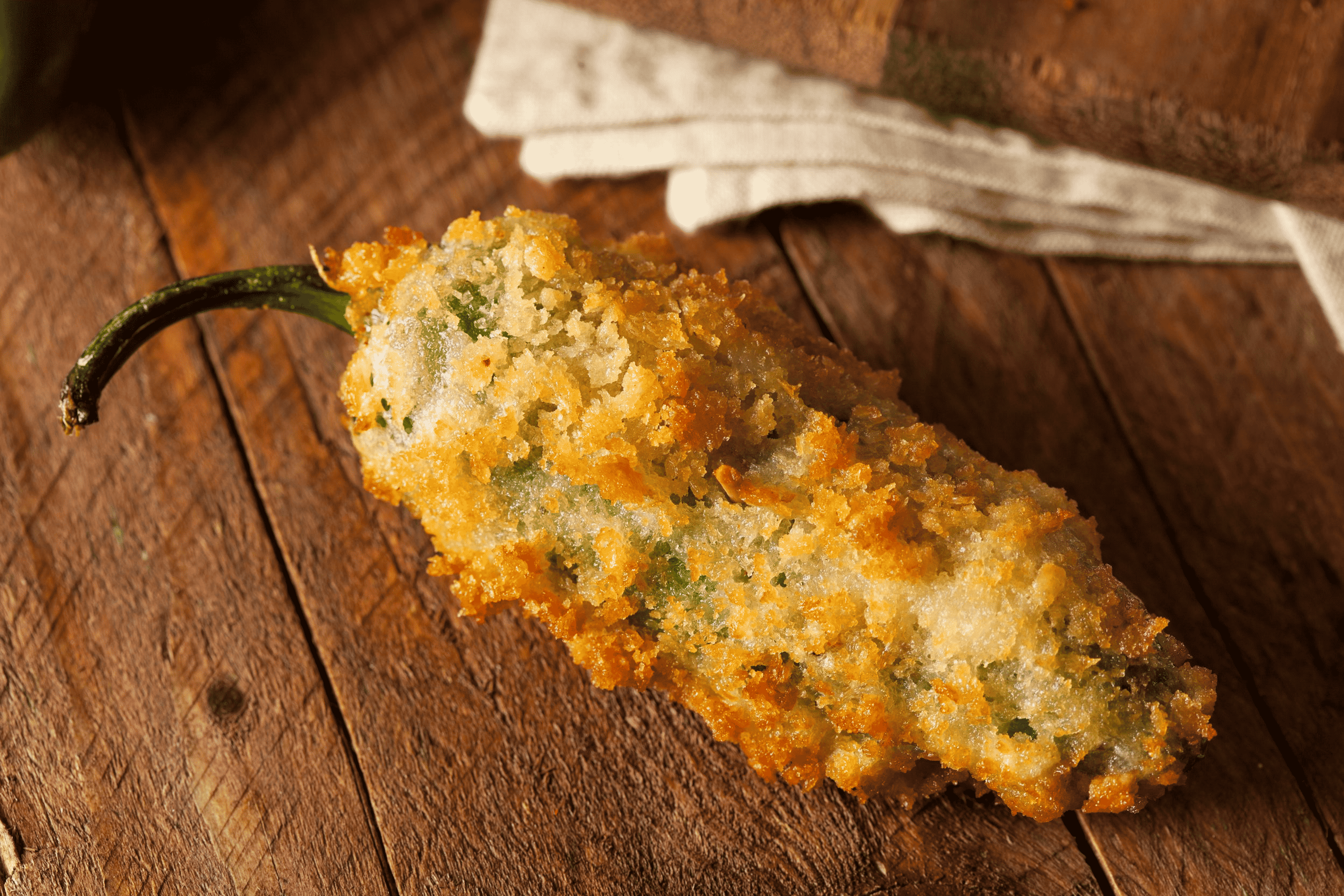 Breaded jalapeño popper with green stem on a wooden board