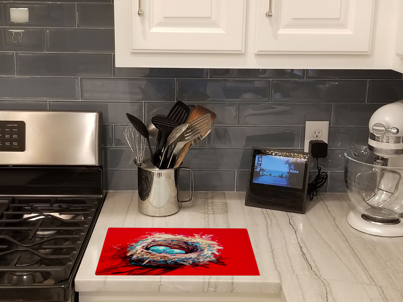 Glass cutting board with bird nest and blue eggs artwork on kitchen countertop