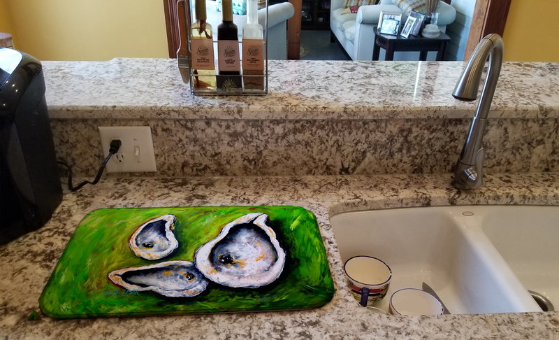 Dish drying mat with green oyster print on countertop near sink