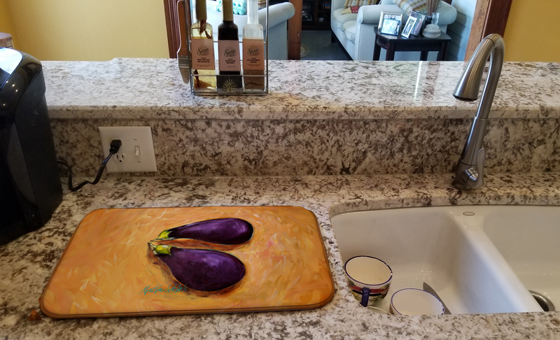 Orange dish drying mat with purple eggplant print on kitchen counter