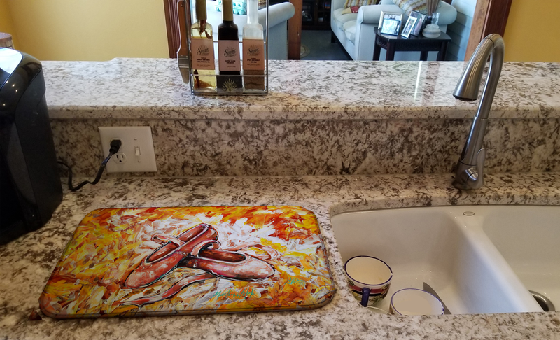 Dish drying mat with colorful ballet-shoe artwork beside a kitchen sink.