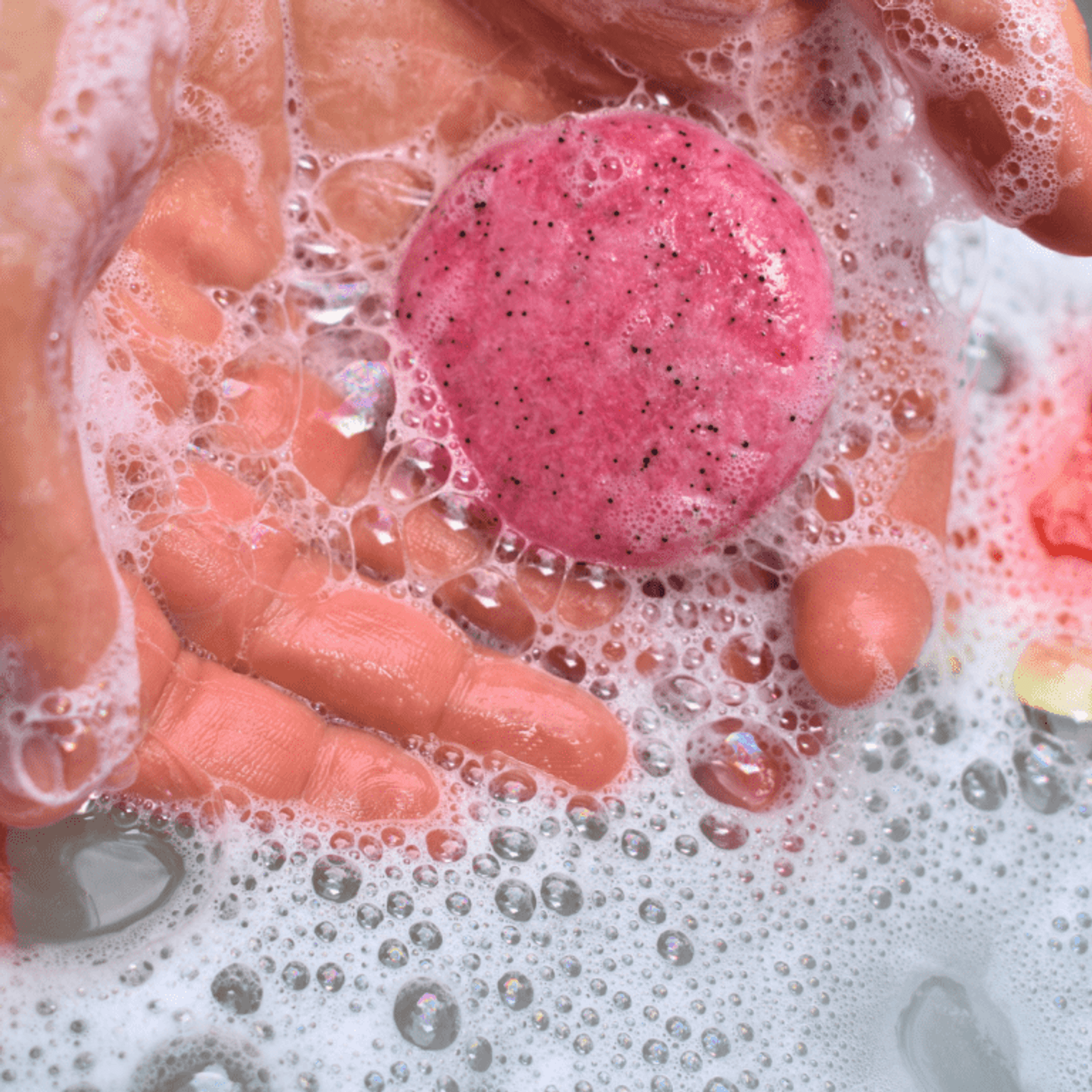 Pink shampoo bar lathering in bubbly water with hands
