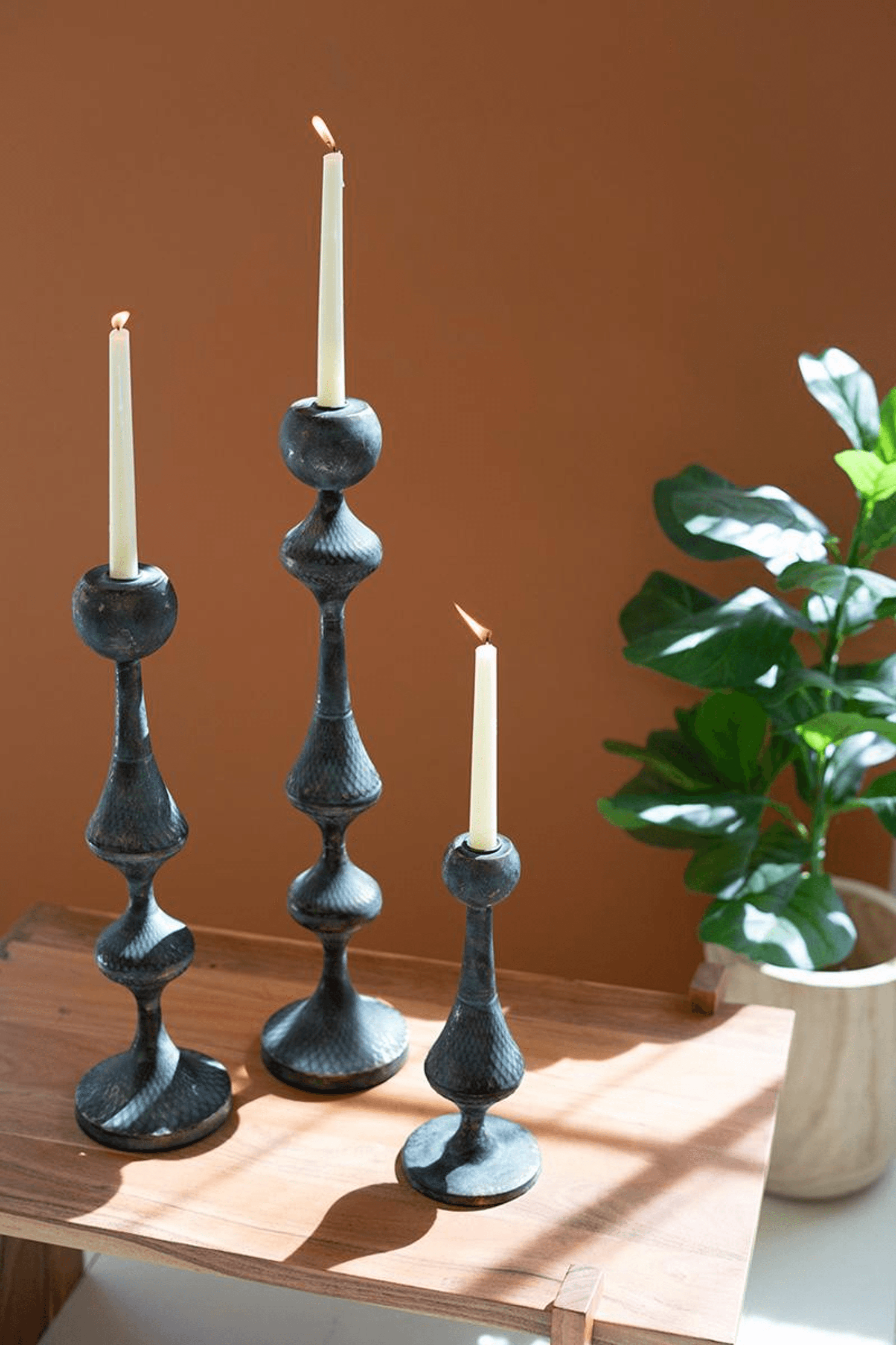 Three metal candle tower holders with white candles, dark blue-gray finish