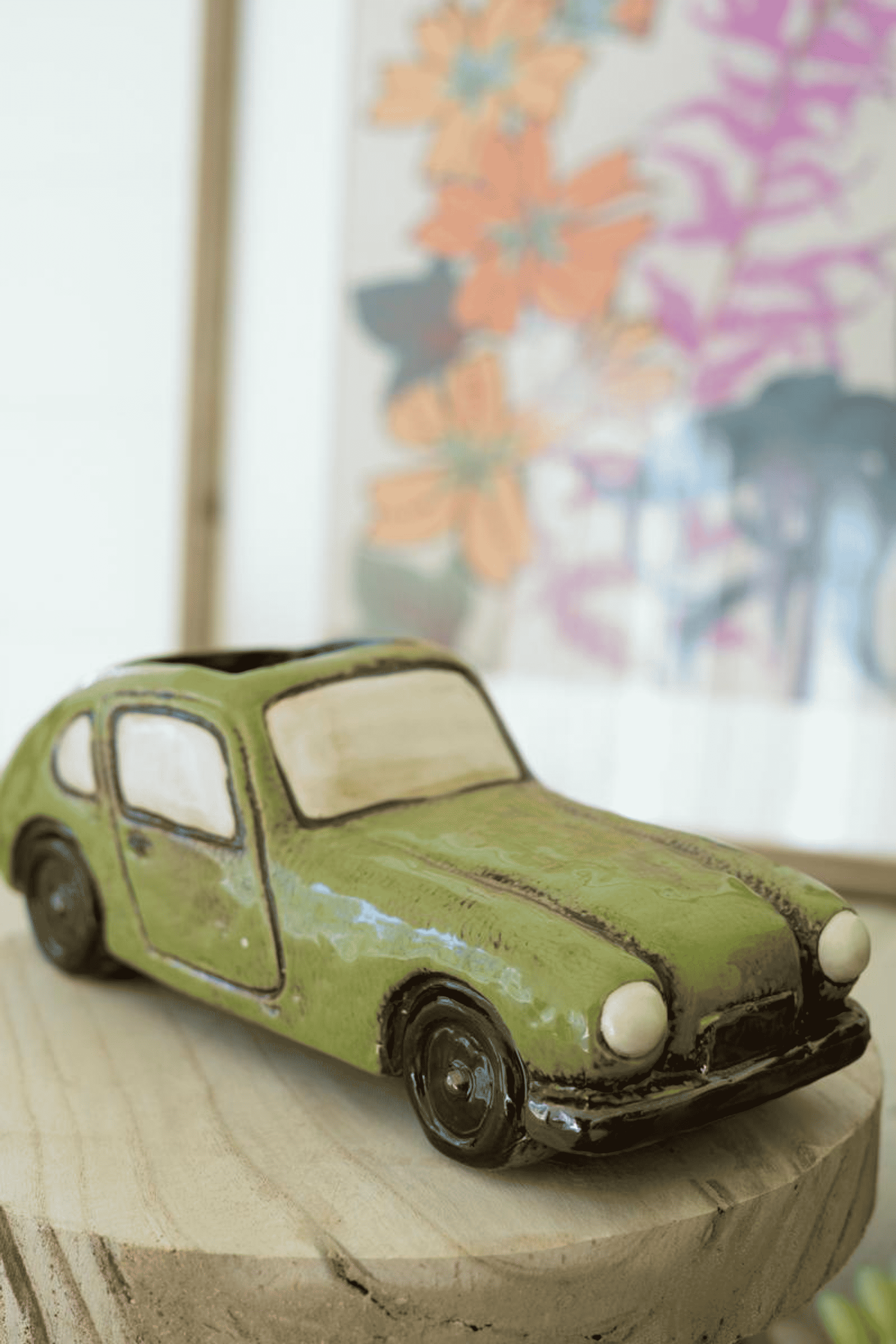 Green ceramic car planter with wheels and open window, holding small plant