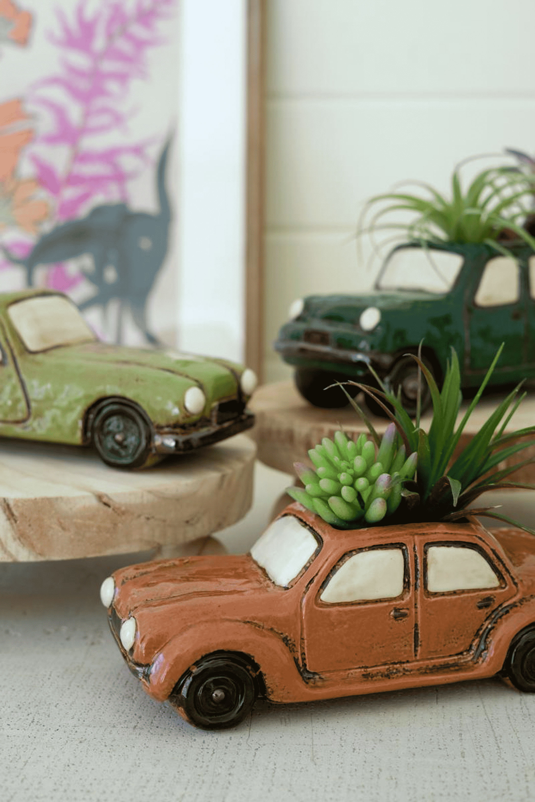 Orange and green ceramic car planters with plants, set on round wooden bases