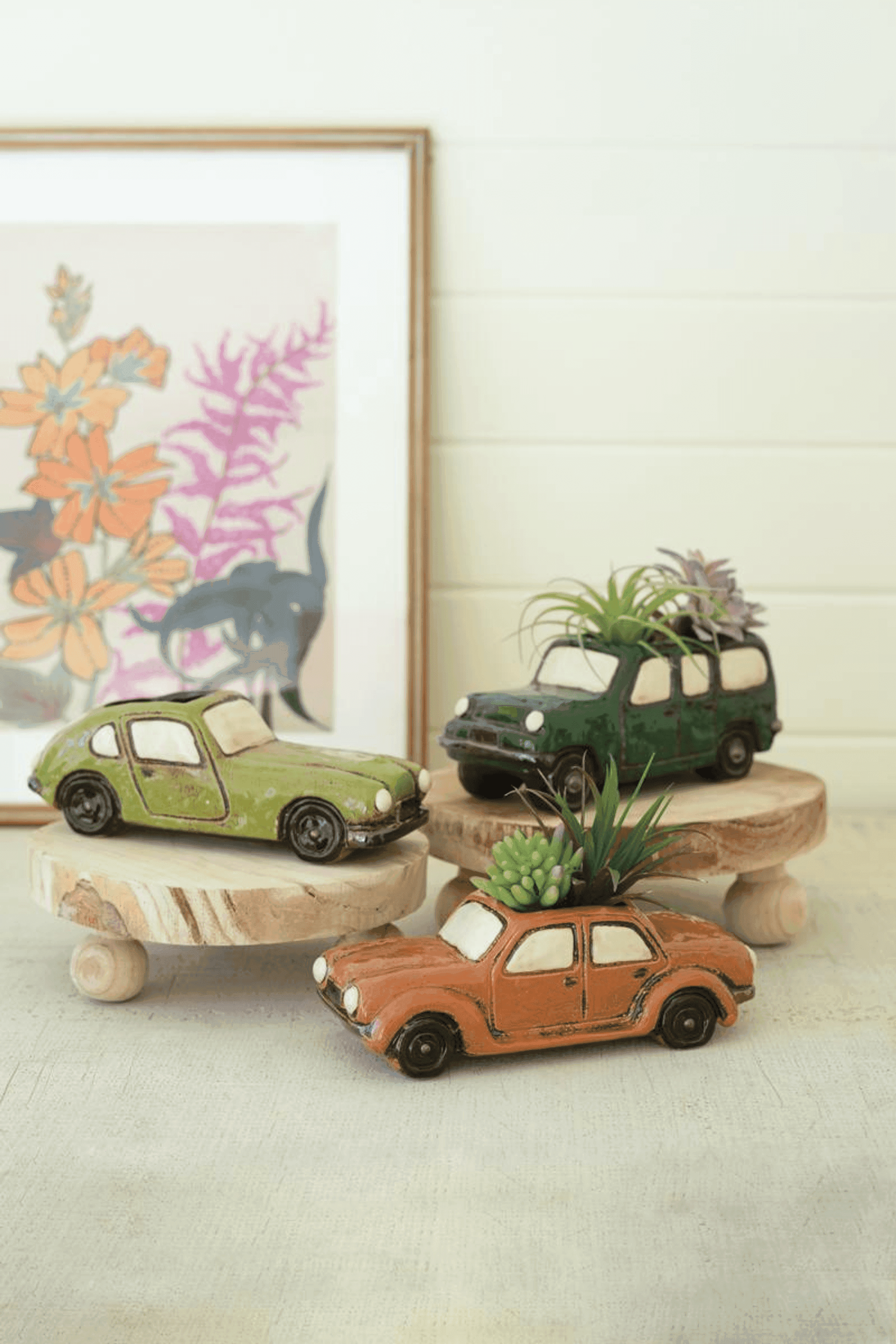 Three ceramic car planters in green, dark green, and orange, each with a plant