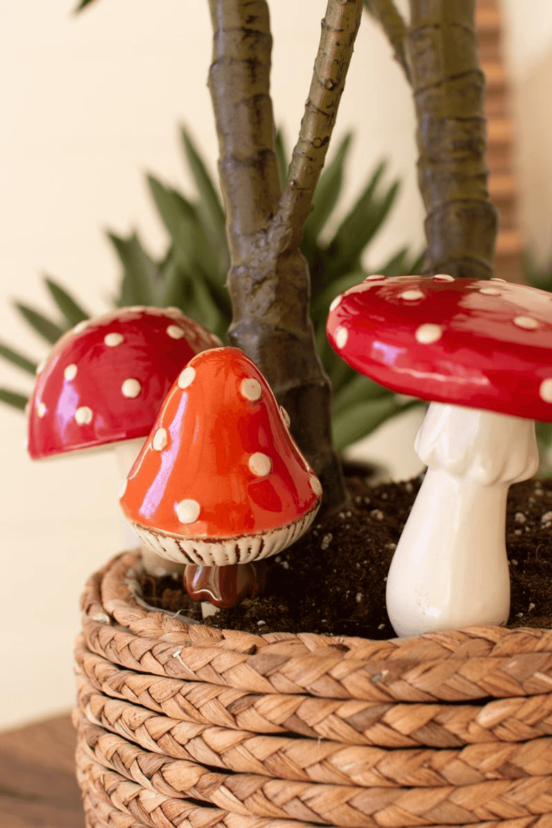 Three ceramic mushroom plant stakes in a woven planter, red caps and white stems