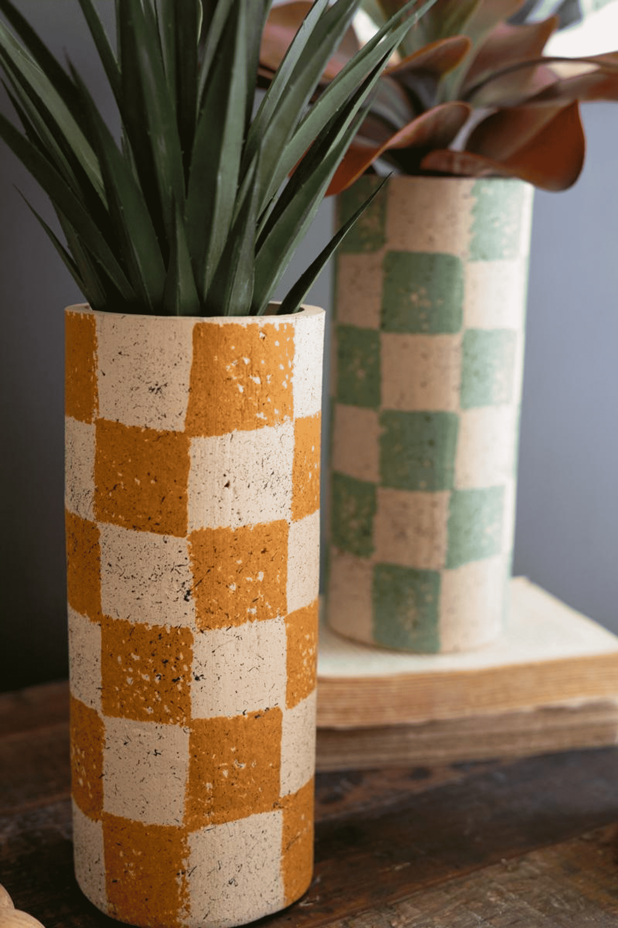 Checked clay cylinder vase in orange-and-cream; second mint-green vase behind
