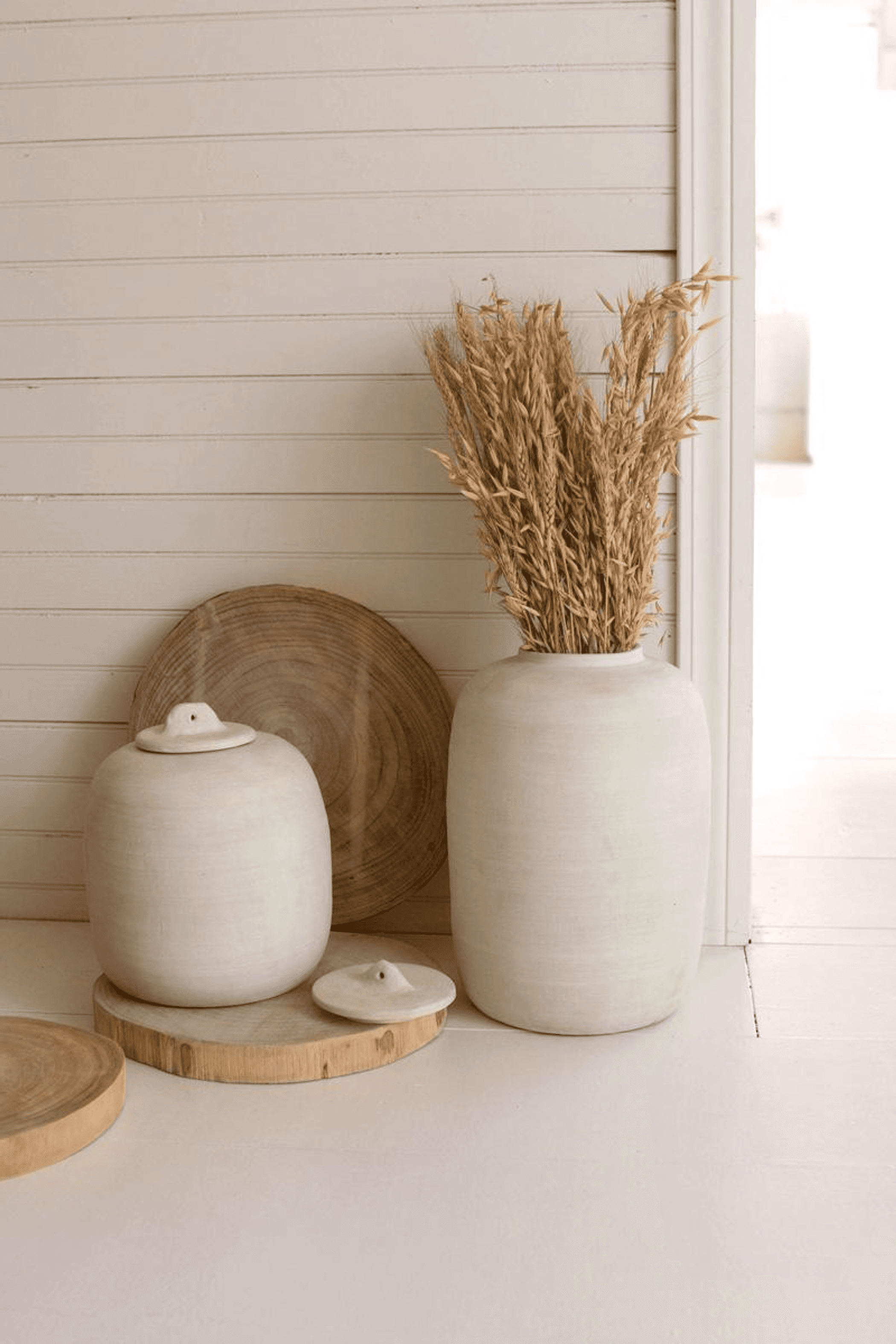 Two off-white ceramic canisters with domed lids on wooden bases, tall and small