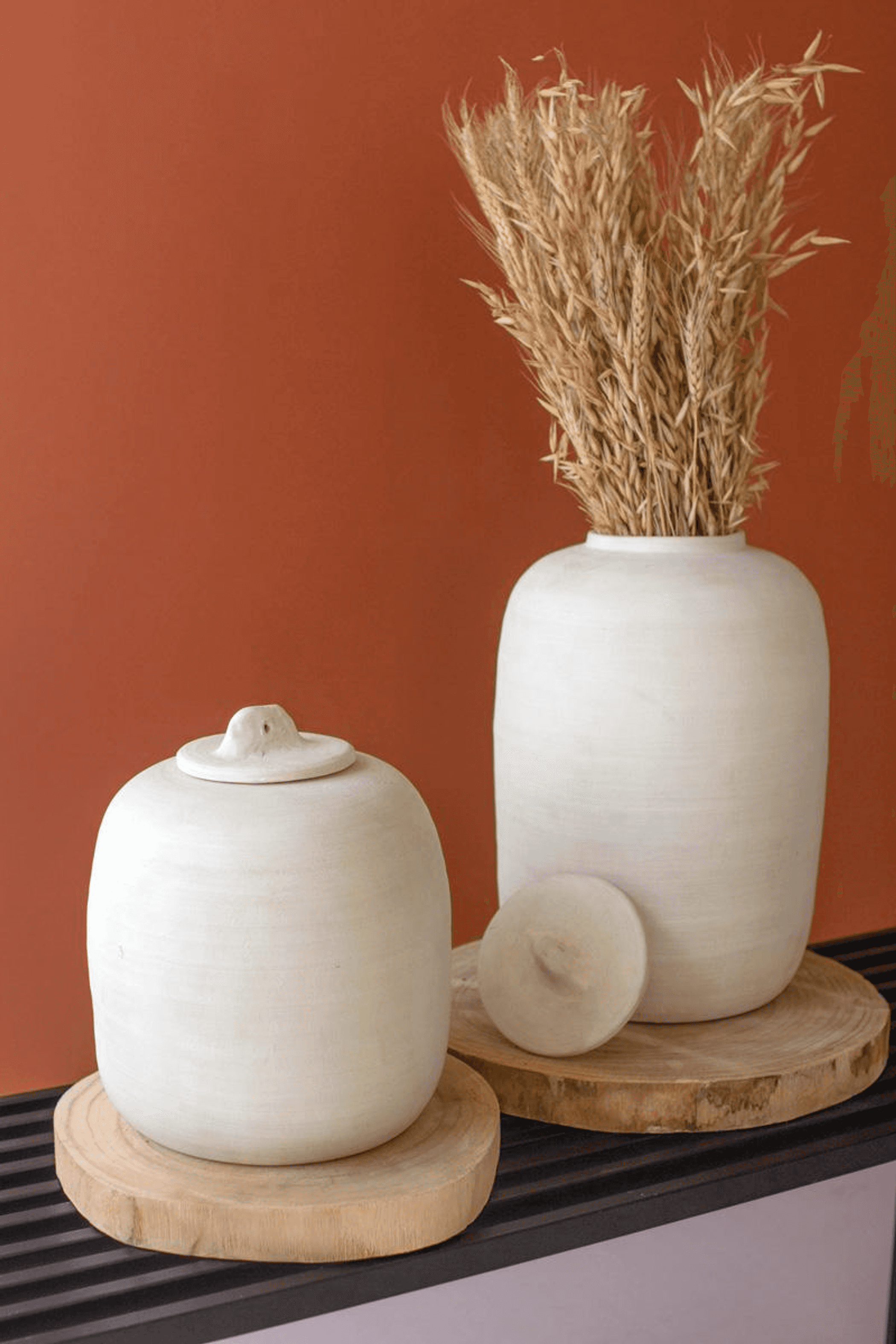 Set of two off-white ceramic canisters with domed lids on wooden bases, tall and small