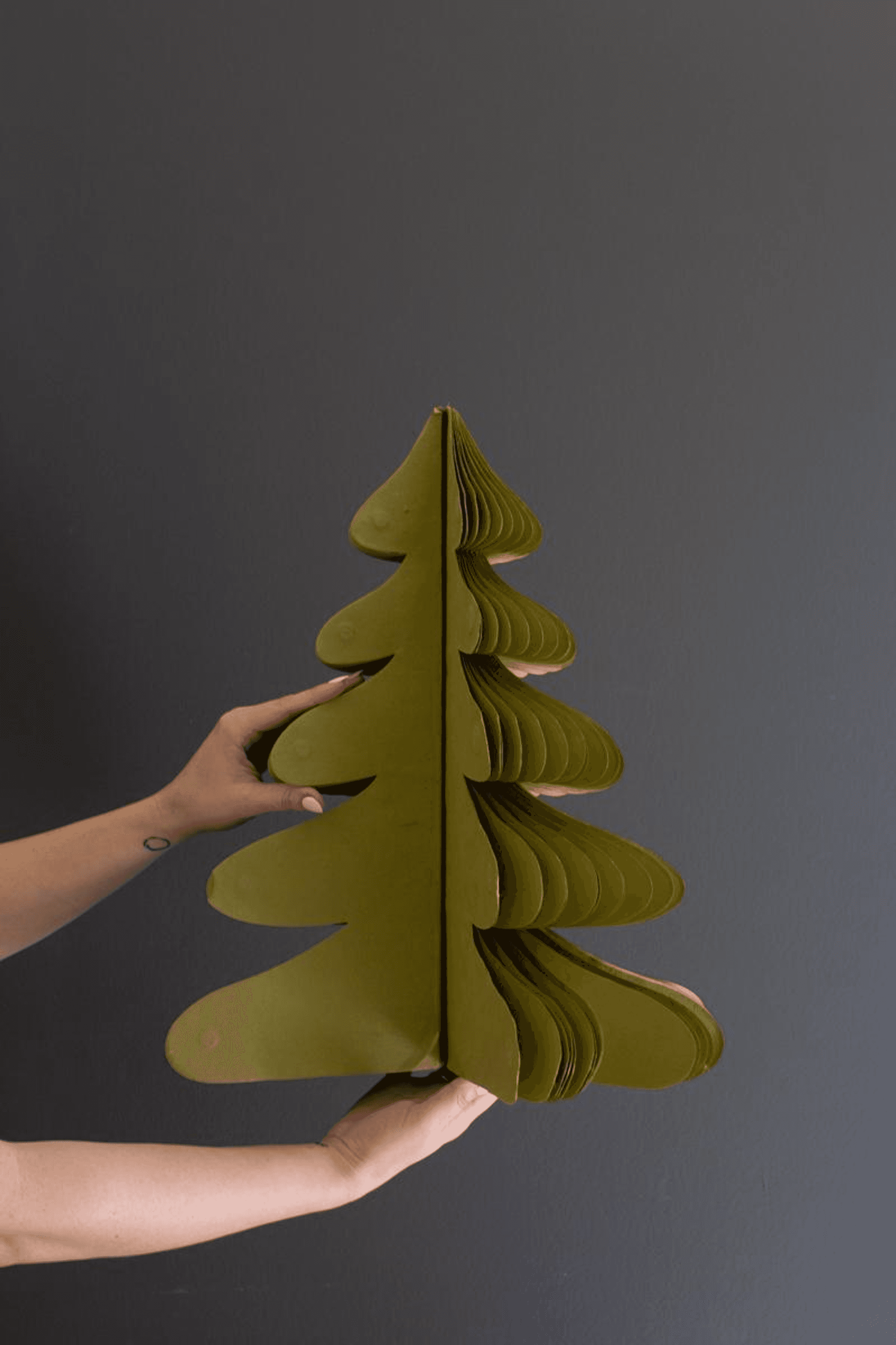 Green paper accordion Christmas tree with layered fold, held open by hands