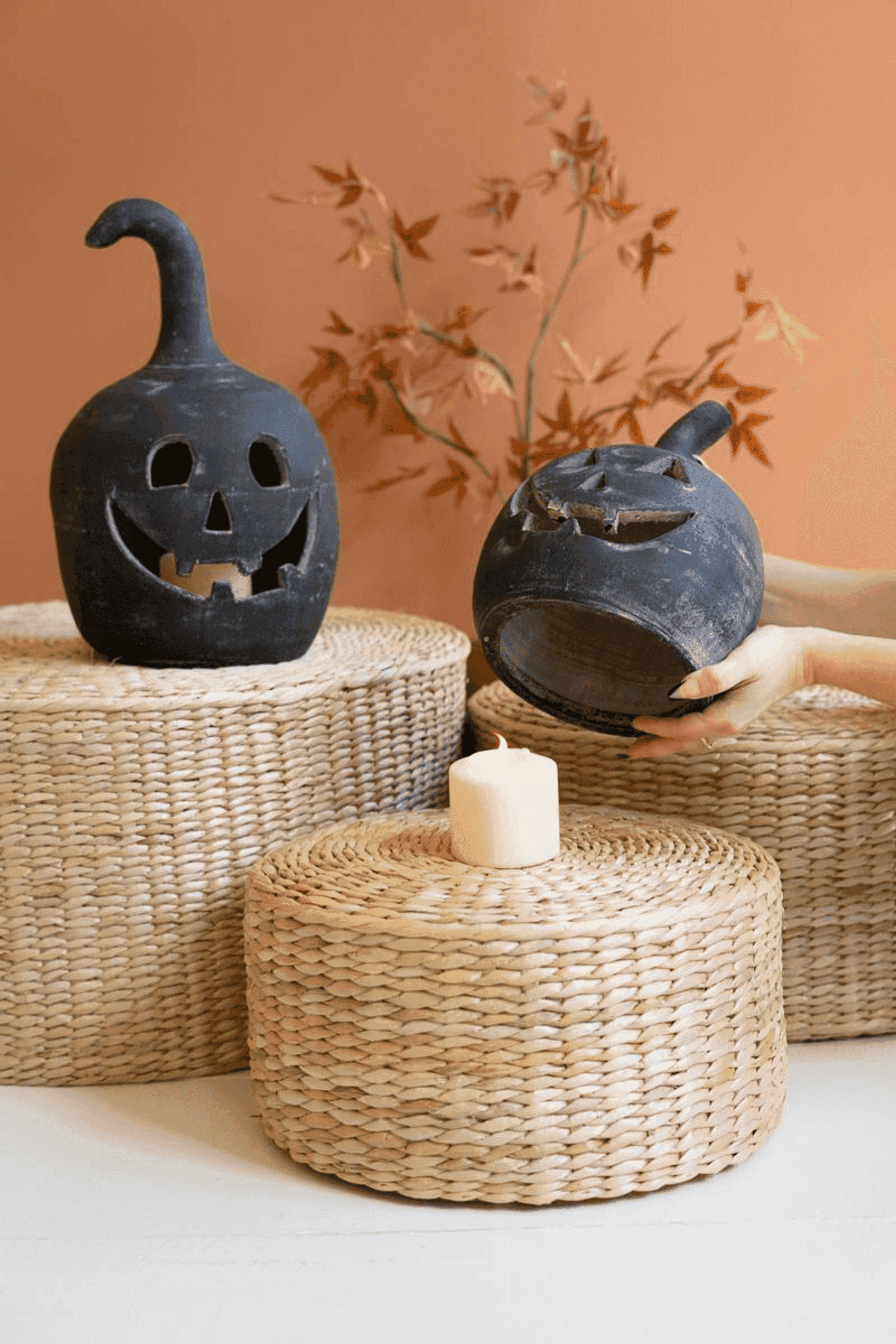 Two black clay jack-o-lantern candle holders with carved faces; one shown held, candle