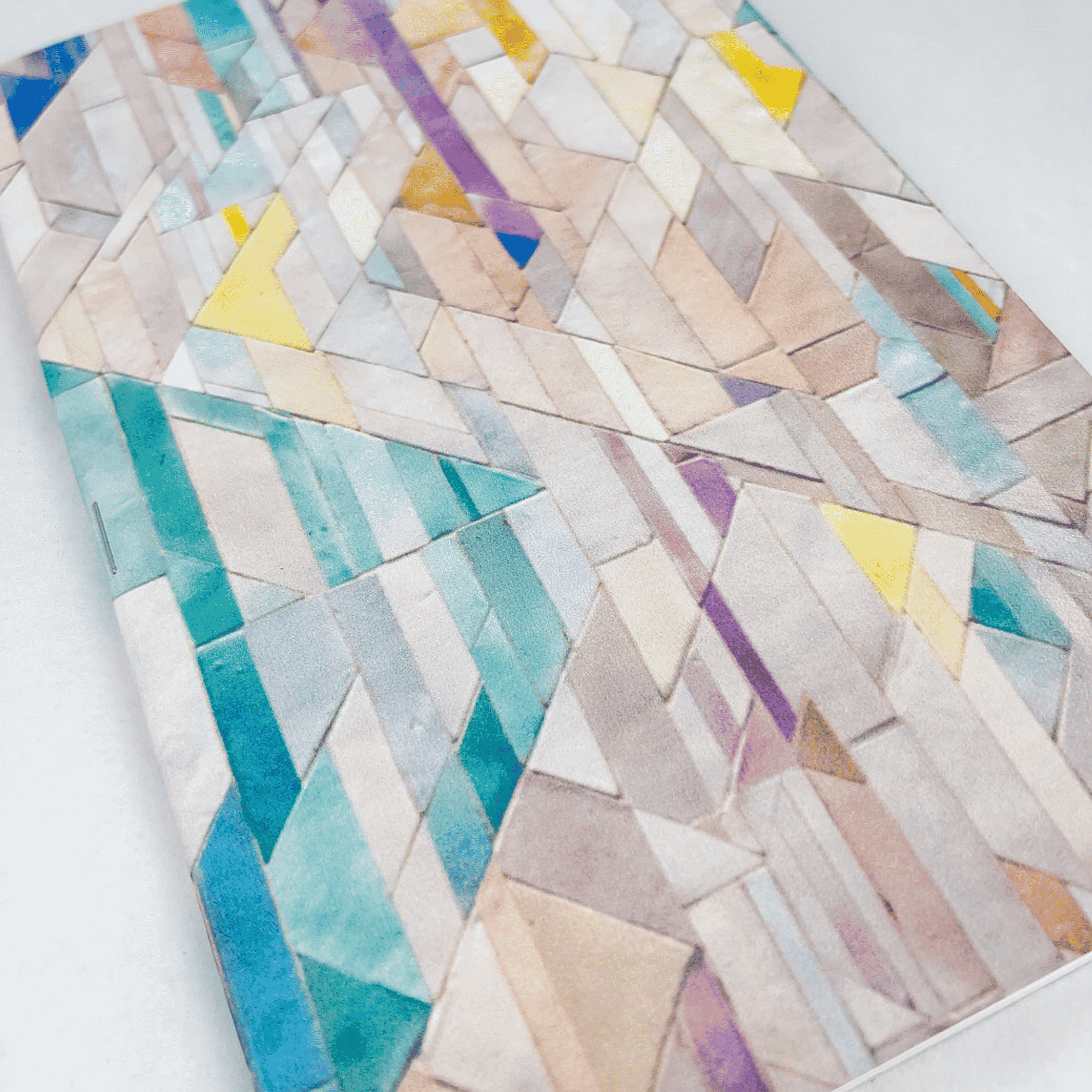 Handmade notebook with multicolor geometric tile cover on a light background.