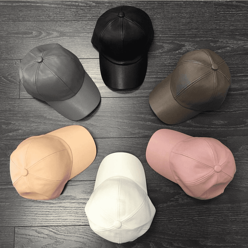 Assorted leather baseball caps on wood, showing black, grey, tan, pink, and white