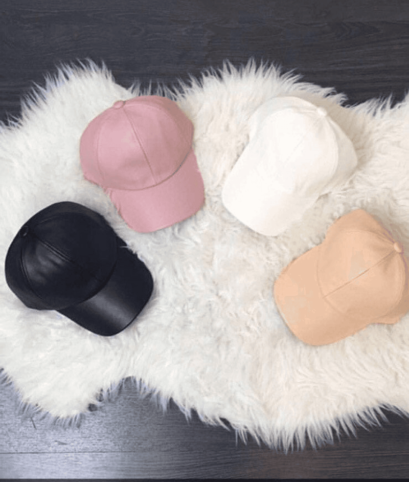 Assorted leather baseball caps on plush surface, including a black cap