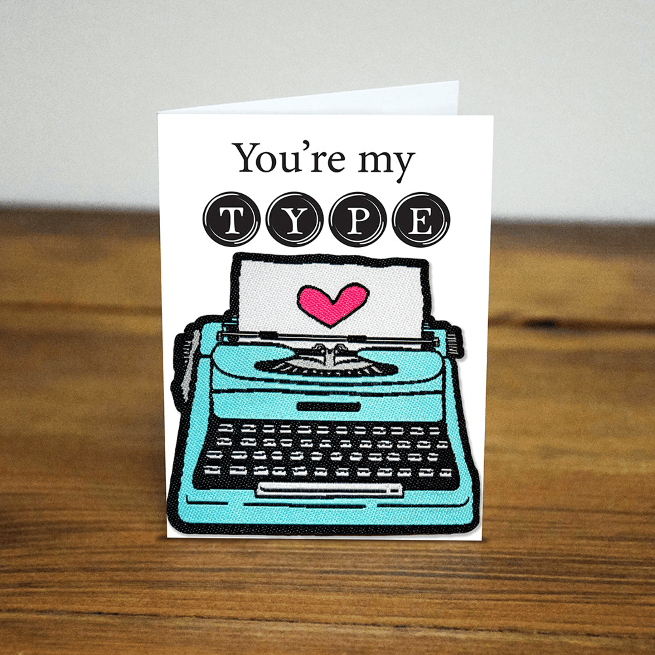 Iron-on patch with cartoon teal typewriter and red heart, surrounded by T Y P E circles