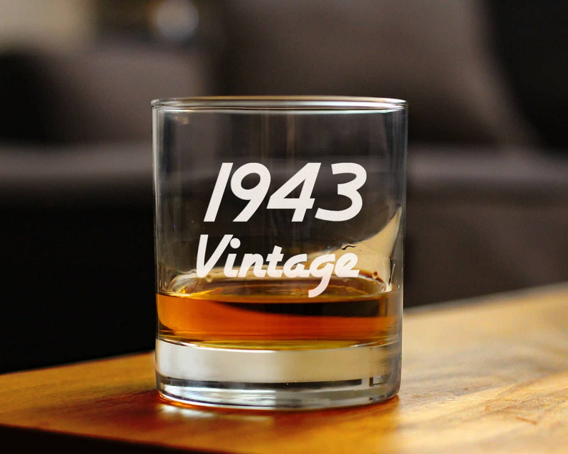 Whiskey rocks glass with etched '1943 Vintage' and amber liquid on table
