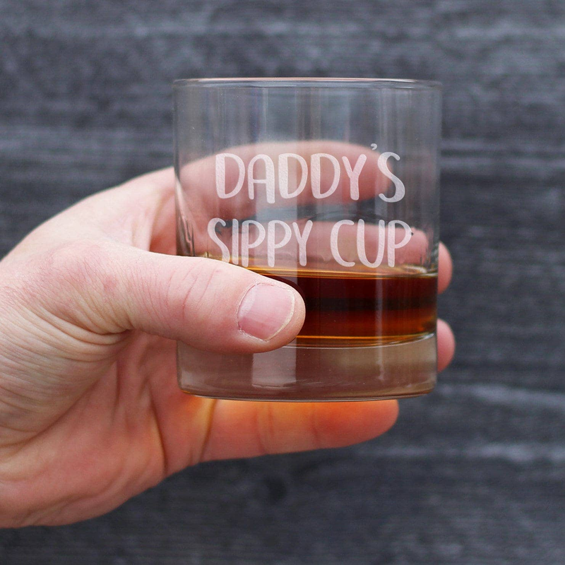 Handheld clear whiskey rocks glass with amber drink and DADDY'S SIPPY CUP etching