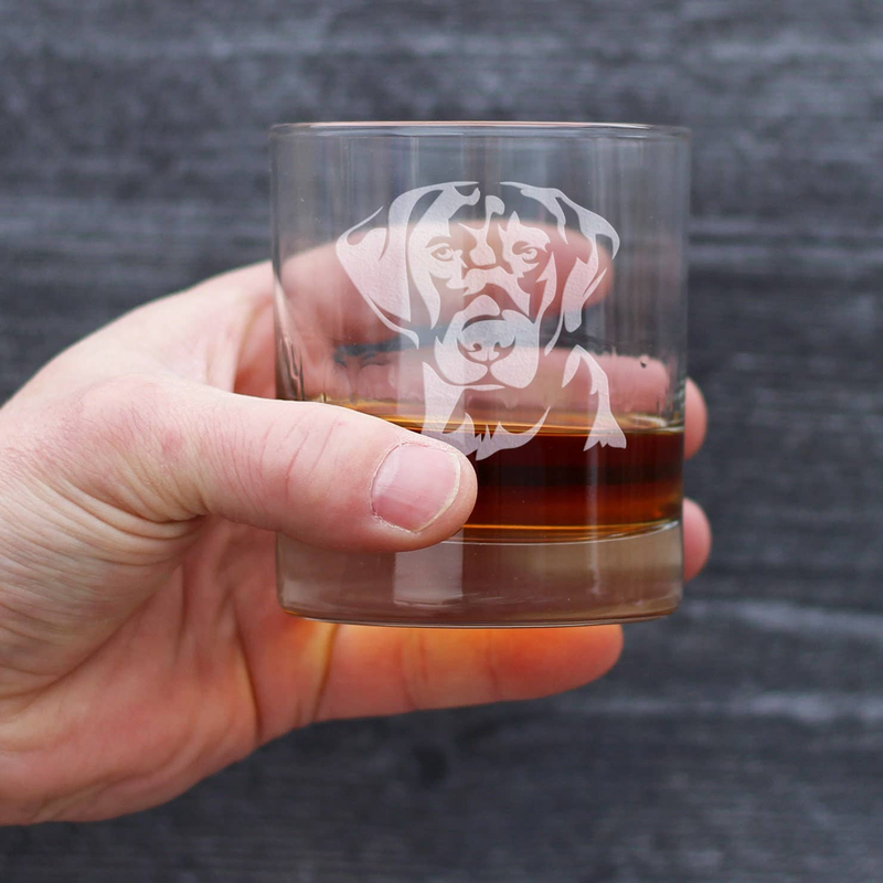 Hand holding clear rocks glass with etched black lab face and amber drink